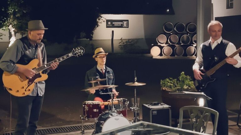 El trío Jazz Because en un ensayo o presentación previa, con guitarras y equipo de música en escena.